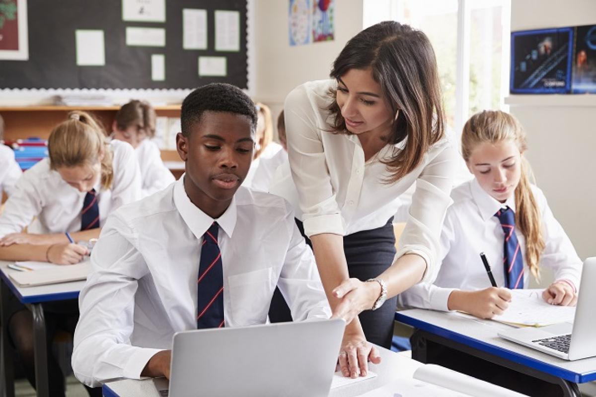 Teacher helps teenage student who is working on a laptop