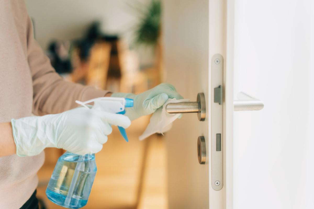 Someone cleaning a door handle with a disinfectant spray